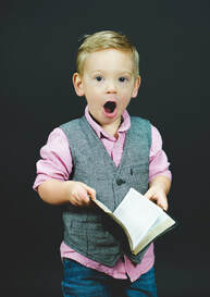Young boy holding a book and showing surprise with his mouth wide open, giving family feedback on a first draft book manuscript.