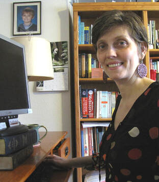 Freelance editor Lynn Post sitting at desk with computer monitor and bookshelf in background.